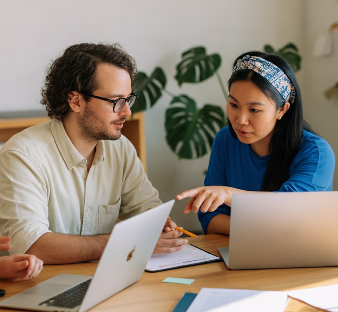 Dois consultores conversando diante de notebooks em uma mesa de trabalho