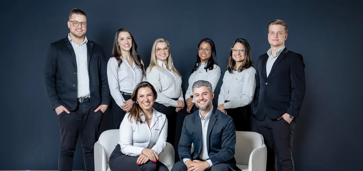 Equipe da Merco: sete pessoas em pé e os sócios Joice e Magnus sentados à frente, diante de uma parede escura